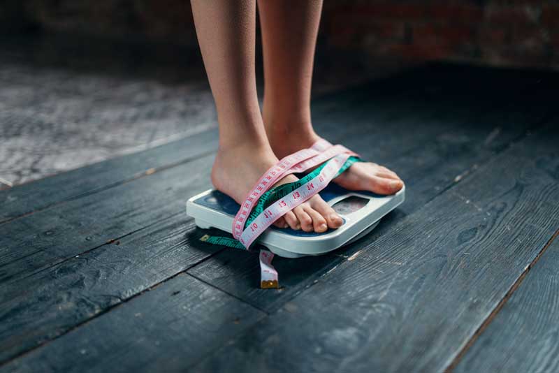 Womans feet on the scales tied with measuring tape